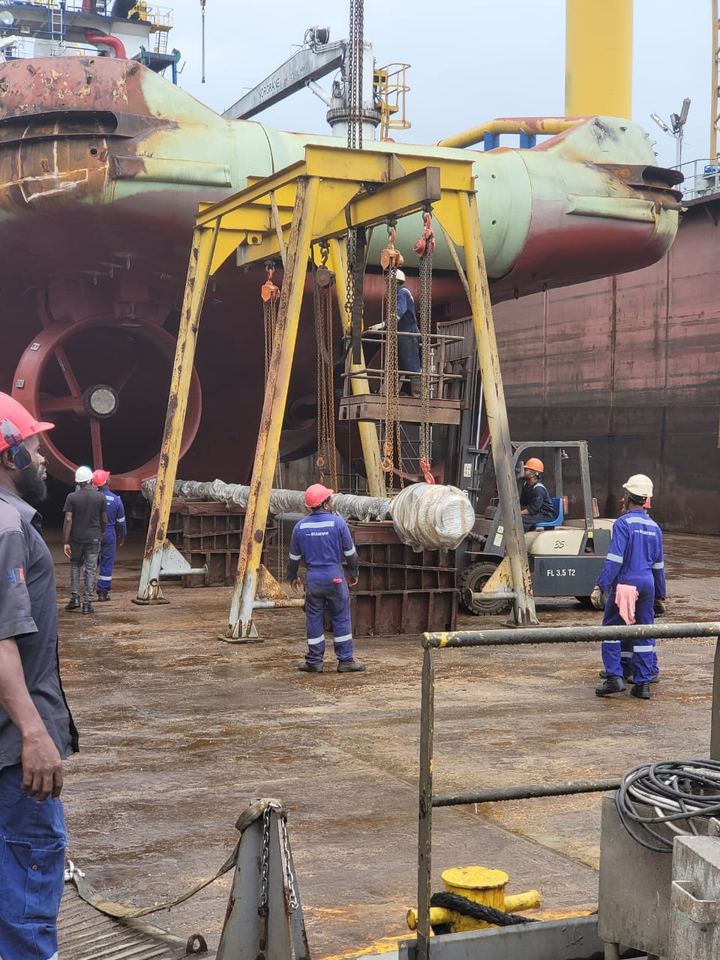 Crew lifting a propeller shaft with a gantry and forklift in dry dock